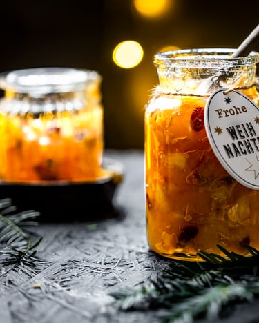 Bratapfelkonfitüre im Glas mit Weihnachts-Etikett, fotografiert von der Seite, vorne liegen Tannenzweige.