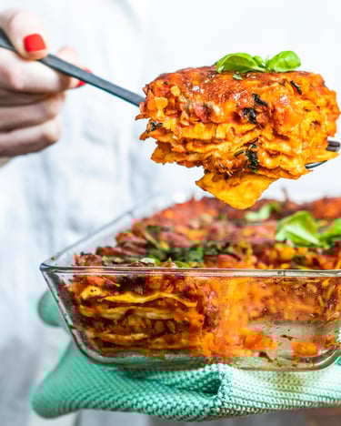 vegetarische Lasagne mit Linsen in gläsernen Auflaufform gehalten von einer Frau mit weißer Bluse