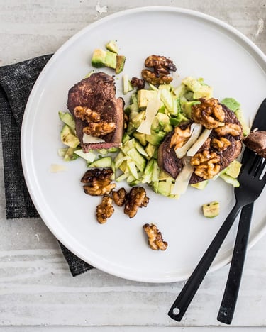 Rinderfilet mit Avocado und Walnüssen auf einem Teller serviert mit schwarzem Besteck.