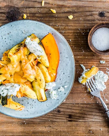 Schupfnudeln mit Kürbis und Zucchini überbacken mit Käse auf einem grau-blauen Teller auf Holzuntergrund.