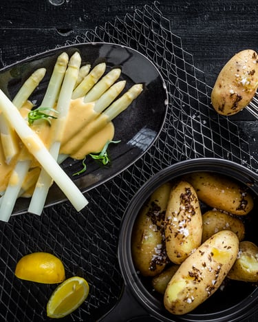 Spargel mit Sauce Hollandaise und Kartoffeln, von oben fotografiert auf einem Servierteller auf dunklem Untergrund.