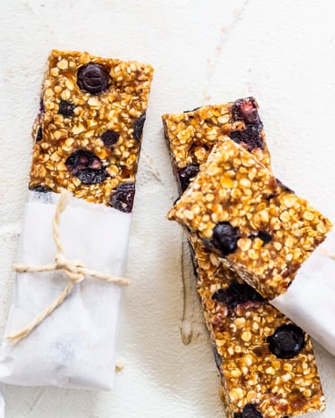Müsliriegel mit Blaubeeren in Backpapier verpackt auf weißem Tisch.