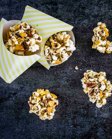 Würzige Popcorn-Kekse in gestreiften Pommestüten auf dunklem Untergrund.