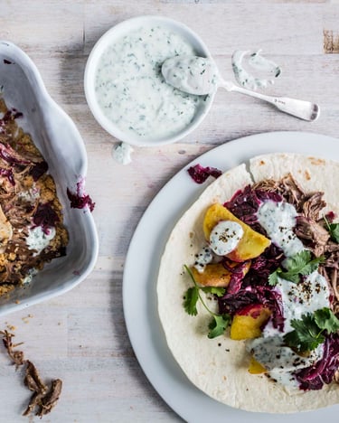 Reste der Weihnachtsgans in Tortillas gerollt mit Sauce, Rotkohl und Kartoffelknödeln serviert in einer Auflaufform.
