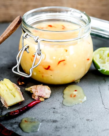 gelbe Chilisauce in Weckglas auf hellem Beton mit Limette und Kochlöffel