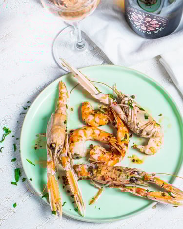 Auf einem weißen Tischtuch sind die gewürzten Scampi auf einem türkisen Teller neben dem Aioli serviert.