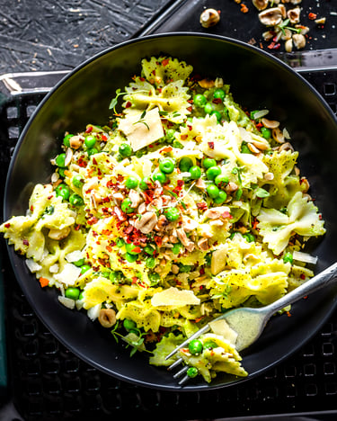 Farfalle mit Joghurt-Erbsen-Sauce und Chiliflocken in einer schwarzen Schüssel serviert mit einer Gabel auf dunklem Untergrund.