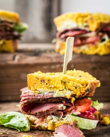 Belegtes Pastrami-Sandwich mit selbst gebackenem gelbem Senfbrot auf Holzuntergrund.