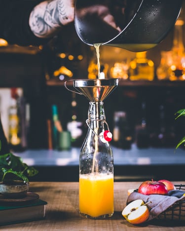 Eine Hand füllt in einer Bar Saft aus einem Topf in eine Flasche mit Korken.