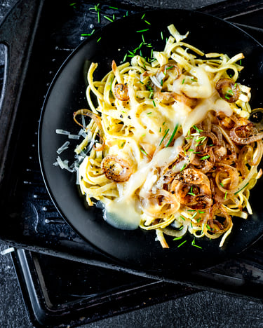 Käsespätzle mit geschmolzenen Zwiebeln auf einem schwatzen Teller.