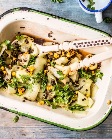 Salat mit Mais, Gurken, Chili und Belugalinsen in einer kleinen Schale mit Salatbesteck.
