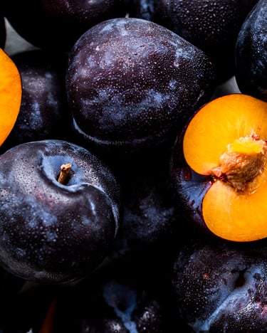 Nahaufnahme von Pflaumen, davon eine Pflaume halbiert mit orangefarbenem Fleisch