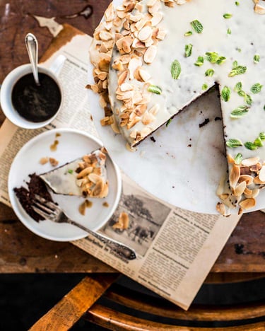 Angeschnittener Kirschkuchen mit Mandeln und Kaffeeglasur neben Kaffeegeschirr und Besteck.