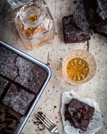 Brownies in einer ofenfesten Form mit einem Glas und einer Flasche Whiskey nebenstehend.