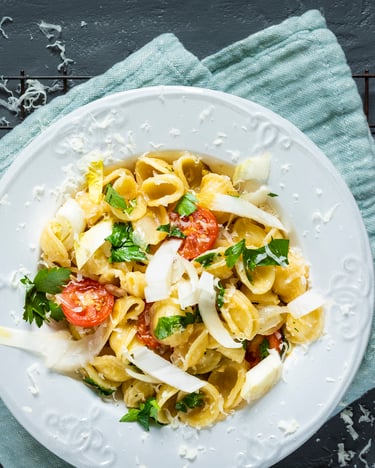 Orecchiette mit Chicorée, Tomaten und Parmesan auf weißem Teller und dunklem Tisch