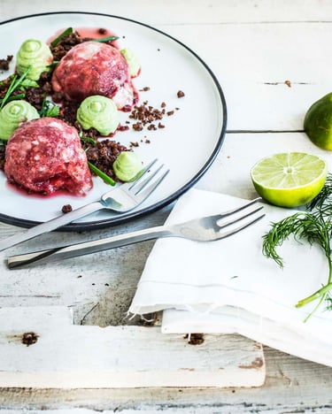 Zwei Kugeln vegane Nicecream aus Banane, Rote Bete und Wassermelone mit Avocado-Limetten-Creme-Tupfen und Pumpernickel auf einem Teller