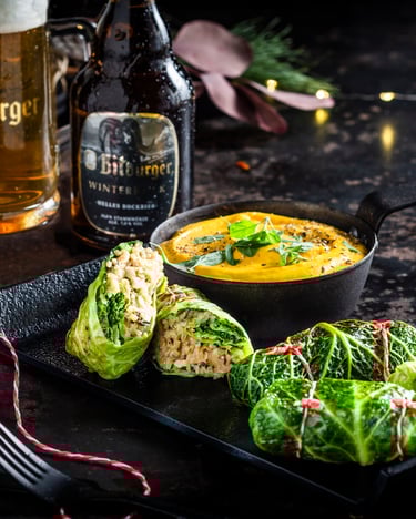 Wirsing-Walnuss-Roulade im Biersud, auf einem Teller, mit Kürbispüree serviert. Bitburger Winterbock steht im dunklen Hintergrund, fotografiert auf dunklem Untergrund.