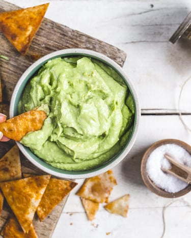 Avocadodip mit Joghurt, daneben Tortilla-Chips und eine Holzschale mit Salz.