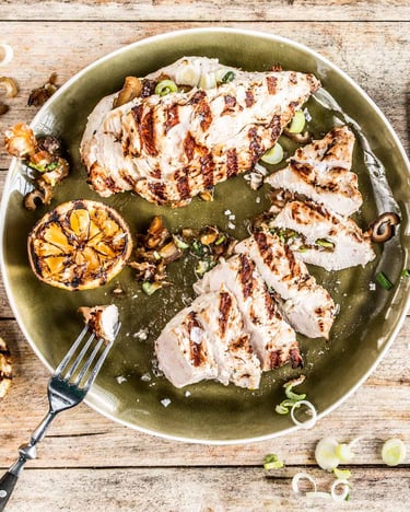 Aufgeschnittenes gegrilltes Hähnchenbrustfiletmi Knoblauch und Zitrone auf einem Teller serviert mit Besteck
