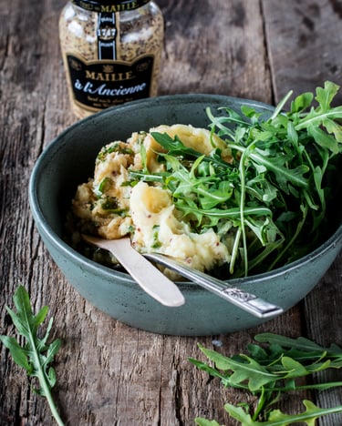 Kartoffelpüree mit Rucola in einer Schüssel mit Besteck neben einem Glas mit körnigem Senf