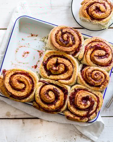 Neun Zwetschgen-Schnecken in heller Backform, zwei Schnecken angestellt auf zwei Tellern