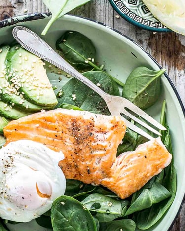 Grüne Bowl mit Baby-Spinat, Lachs, Avocado und pochiertem Ei auf Holztisch