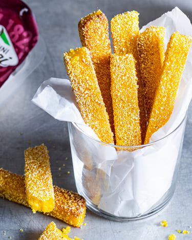 Polentasticks in Glas mit Pesto und Käse im Hintergrund