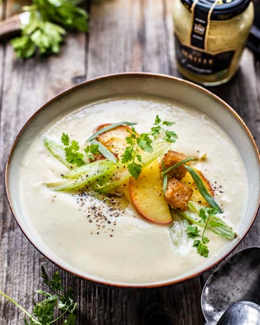 Sellerie-Apfel-Suppe mit Brotwürfeln, Apfelspalten und Kräutern.