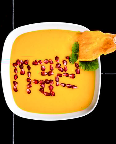 Kuerbissuppe Mit Granatapfelkernen in einer weißen Schale auf schwarzen Fliesen