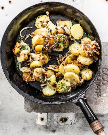 Bratkartoffeln mit Käse und Zwiebeln in Pfanne auf hellem Untergrund