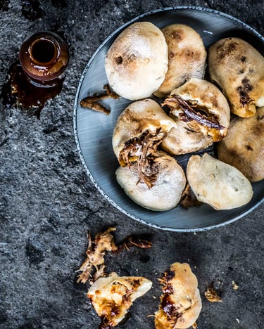 Pulled Pork Pizzabrötchen auf einem Teller und dunklem Untergrund, daneben ein Fläschchen BBQ-Sauce.