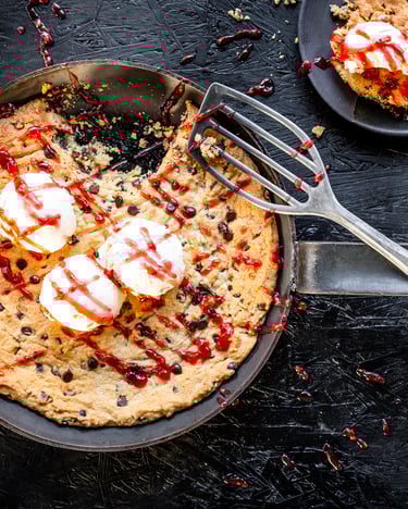 Goldbrauner Riesen-Cookie mit Vanilleeis und Himbeersauce in einer Pfanne auf einem dunklen Hintergrund.