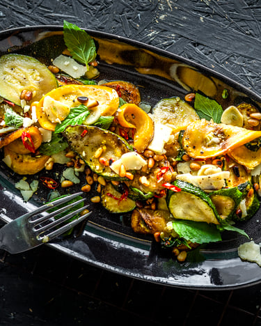 Zucchini-Salat mit Minze und Pinienkernen auf einem schwarzen Teller.