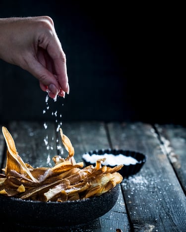 Pastinakenchips in Schüssel, die mit Salz aus der Hand bestreut werden.