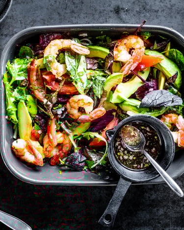Avocado-Salat mit Garnelen mit Dressing in kleiner Schale auf grauem Untergrund