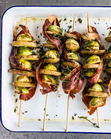 Rosenkohl mit Schinken und Kartoffeln aufgespießt in einer Auflaufform.