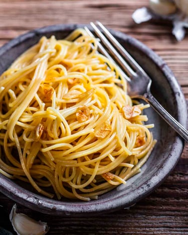 Spaghetti aglio e olio mit Knoblauchchips auf grauen Teller mit dunklem Holzuntergrund