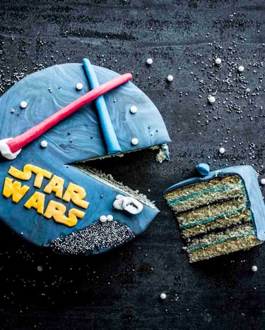 Angeschnittene blaue Star-Wars-Torte mit Laserschwertern und Star Wars Schriftzug auf dunklem Untergrund