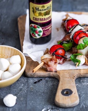 Melonenspieße mit Parmaschinken, Tomaten und Mozzarella auf einem Holzbrett mit Balsamicocreme verziert