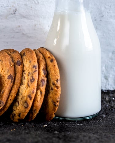 Chocolate Chip Cookies aneinander gereiht mit einer Glasflasche Milch.