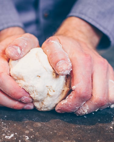Teig der Pizza Margherita wird auf Arbeitsfläche von Hand durchgeknetet