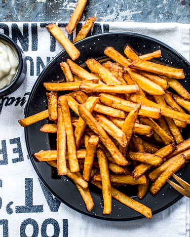 Pommes auf dunklem Teller mit angesteller Mayonnaise in Schüsselchen