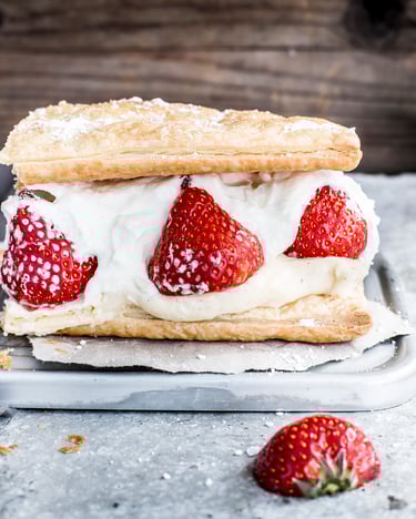 Zwei Blätterteigscheiben sind gefüllt mit einer Sahnecreme und frischen Erdbeeren.
