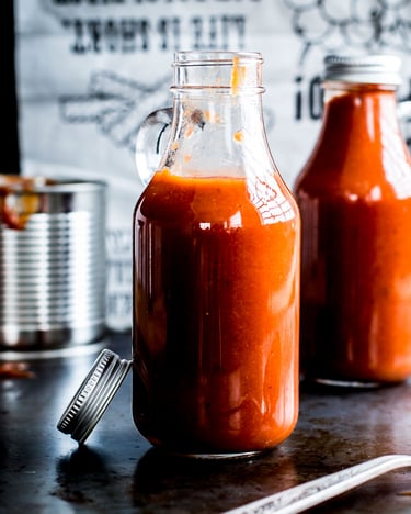 Zwei Glasflaschen mit Rhabarber-Tomatenketchup auf schwarzer Arbeitsfläche mit Blechdose
