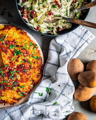 Rösti trentino mit Speck auf Teller mit Krautsalat, Kartoffeln und Geschirrtuch.
