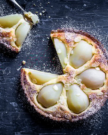 Goldgelb gebackene Mandeltarte mit Birnen auf einem dunklen Hintergrund.
