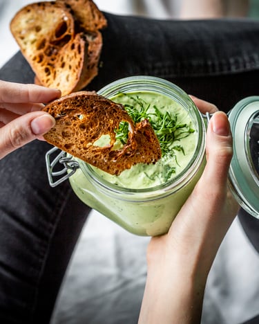 Avocado-Basilikum Dip in einem Einmachglas, dazu geröstetes Brot, was in den Dip gedippt wird.