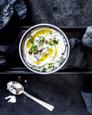 Frischkäse-Dip mit roten Zwiebeln in Schale auf schwarzem Tisch mit schwarzer Kohle.
