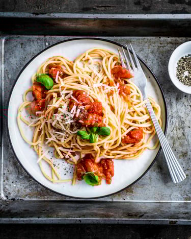 Spaghetti mit Tomatensoße auf einem weißen Teller auf einem Metalltablett.
