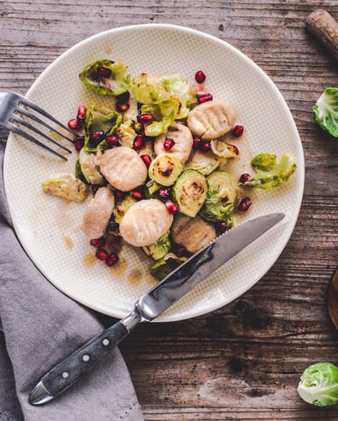 Gnocchi mit Rosenkohl und Granatapfelkernen auf einem weißen Teller mit Besteck angelegt.